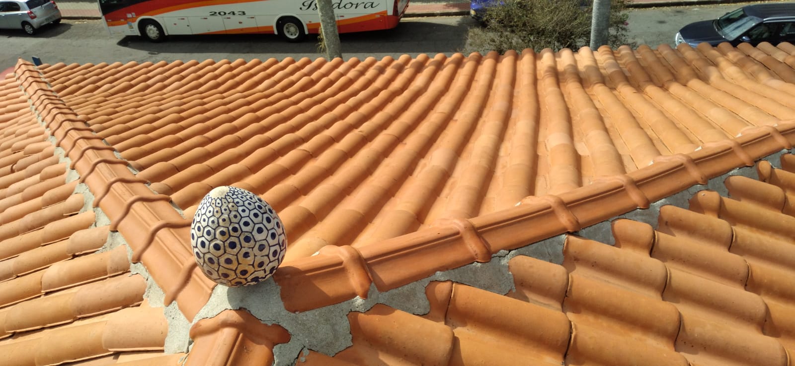 Telhado residencial de cerâmica recém lavado, com telhas laranjas vibrantes e pomba decorativa, demonstrando o resultado do serviço de lavagem.