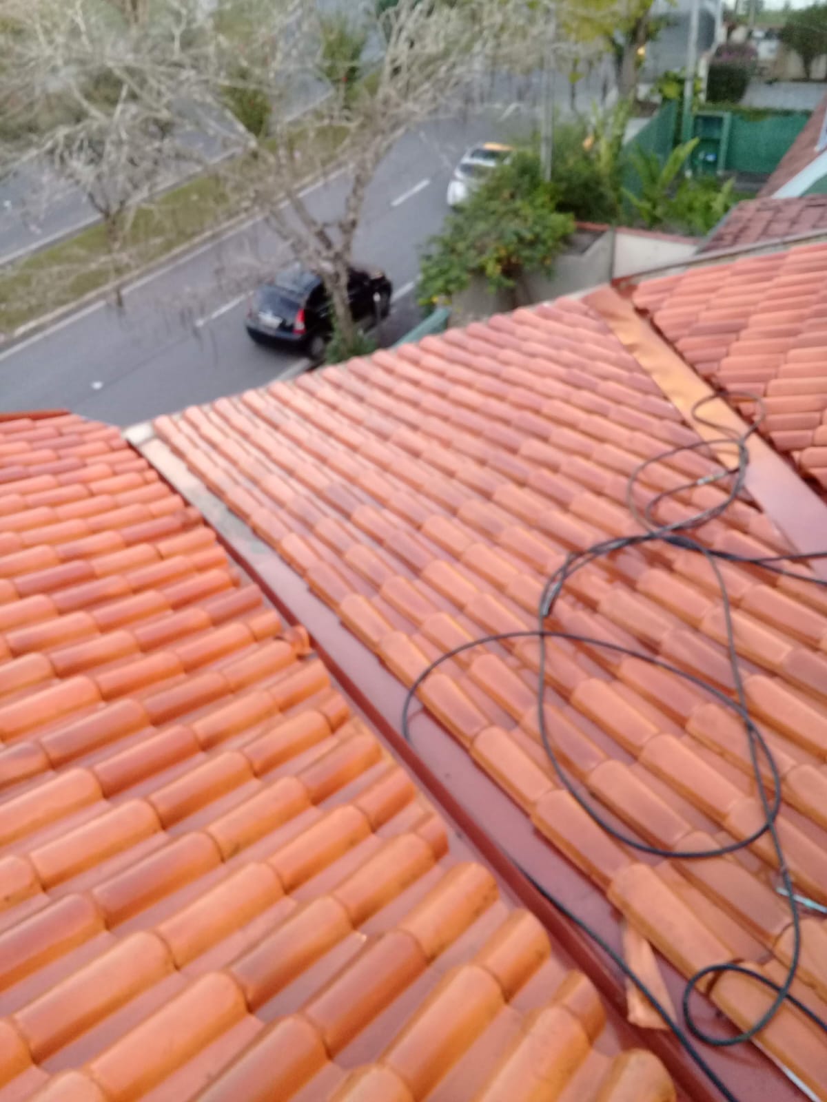 Telhado residencial recém lavado com telhas de barro laranja, com mangueira ainda sobre o telhado mostrando o serviço recém finalizado